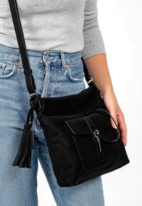 Schwarze Umhängetasche aus strukturiertem Stoff mit einer Fronttasche und einem Quastenakzent. Verfügt über ein schlankes Design und einen verstellbaren Riemen.