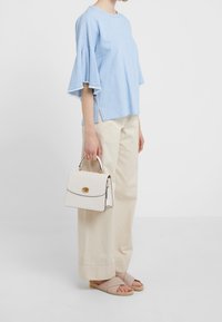 Ljusblå bomullstopp med trumpetärmar, krämfärgade vida byxor och beige sandaler. Vit handväska med guldiga detaljer och spänne.