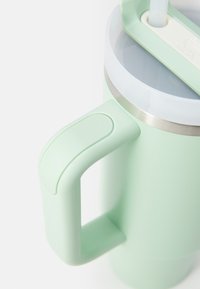 Tazza da viaggio verde menta con manico curvo, accento in acciaio inossidabile nella parte superiore e un coperchio con beccuccio dotato di cannuccia e meccanismo di chiusura.