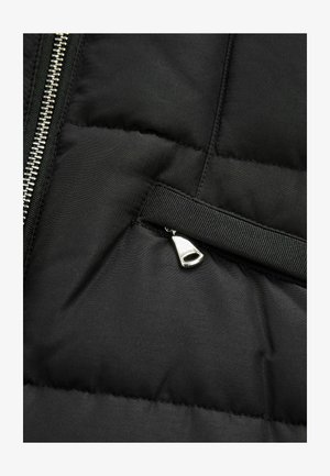 Mustast puffermantlist valmistatud kangast, millel on tikitud tekstuur, hõbedane tõmblukk ja must võrgusilma tõmbeustega külgmise õmbluse lähedal.