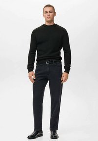 Maglione nero a maglia abbinato a jeans scuri. Il modello indossa una cintura nera e stivali in pelle nera. Texture liscia, design aderente, stile minimalista.