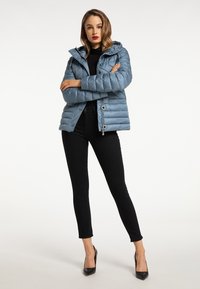 Giacca puffer azzurra con cappuccio, con zip frontale e bottoni a pressione, abbinata a pantaloni neri a gamba aderente e tacchi neri.
