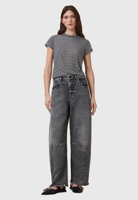 T-shirt à col rond rayé en noir et blanc, associé à un jean gris délavé, taille haute et coupe large, ainsi qu'à des chaussures plates noires.