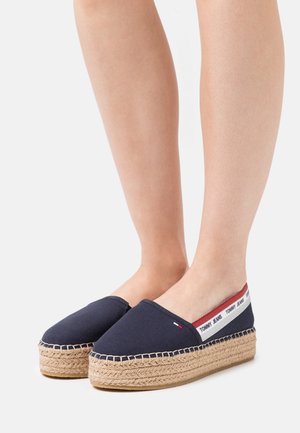 Laivastonsiniset kanvas espadrillot kudotulla jute-pohjalla, joissa on punavalkoinen logonauha kantapäässä ja pyöreä kärki.