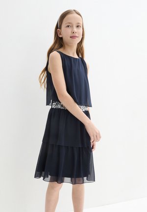 Abito svasato blu navy con sovrapposizione trasparente e cintura accentuata da paillettes. Presenta un design senza maniche e una texture di tessuto morbido.