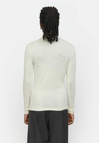 Helles graues Langarmshirt aus weichem, enganliegendem Stoff. Verfügt über einen runden Halsausschnitt und eine glatte Textur. Kombiniert mit grauen Hosen.