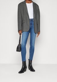 Grå oversize blazer, vit t-shirt, blå skinny jeans, svarta läderankelstövlar och en liten svart väska med minimalistisk design.