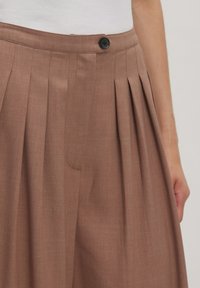 Braune, gefaltete Hosen aus leichtem Stoff, mit einem Knopfverschluss vorne und seitlichen Taschen. Strukturierte Oberfläche mit maßgeschneiderter Passform.