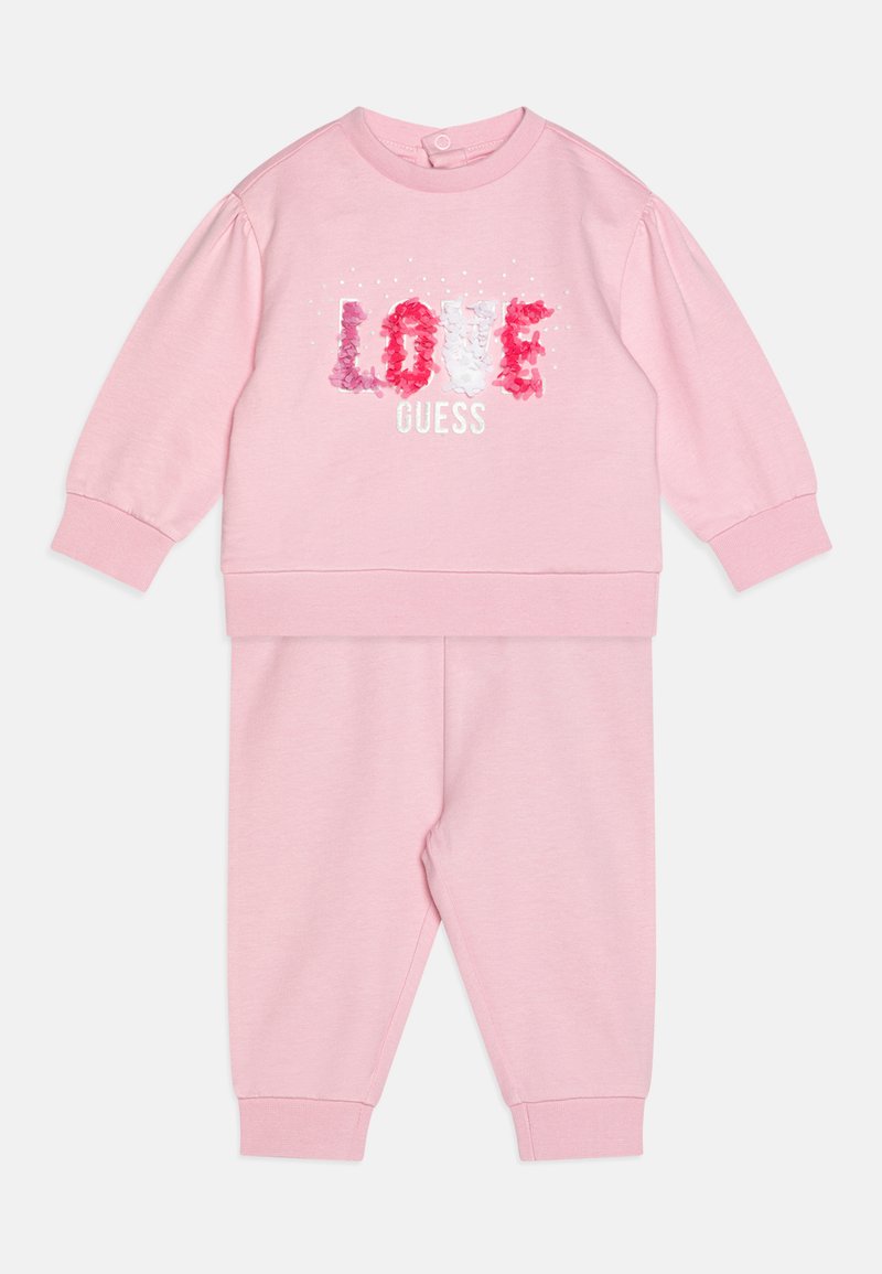 Rausvas medvilnės sportinis kostiumas su "LOVE GUESS" tekstu ir gėlių akcentais. Yra briaunoti rankogaliai ir apvalus kaklas. Minkšta tekstūra.
