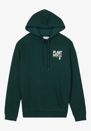 Dark green cotton hoodie with a front pocket, drawstring hood, and white print design reading "PLANT SHOP." Soft texture and relaxed fit.