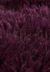 Plysset lilla shag tæppe med lange, bløde fiber, der skaber en tekstureret overflade; den rige, dybe farve komplementerer den tykke, luksuriøse fornemmelse.