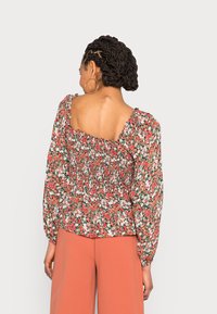Blusa floral em vermelho, verde e branco, com decote quadrado, mangas bufantes e cintura franzida; combinada com calças largas pêssego.