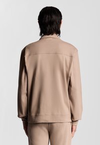 Beige sweatshirt med rund krage, sänkt axel och ribbade ärmar. Slät textur med minimalistisk design och etikett på baksidan.