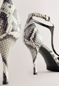 Sandales à talons avec un motif peau de serpent noir et blanc. Elles sont dotées d'une bride de cheville avec une boucle et d'un talon stiletto haut et fin.