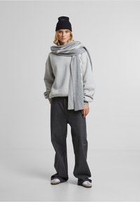 Grå oversized sweatshirt, mørke brede jeans, grå tørklæde og sort strikket hue. Hvid tekstmønster på tørklædet, glat tekstur, afslappet stil.