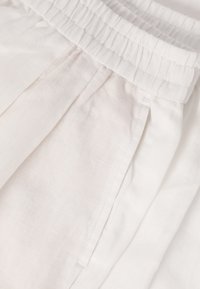 Gros plan d'un pantalon blanc en tissu léger présentant une ceinture élastique et une poche de couture latérale avec des détails de coutures visibles.