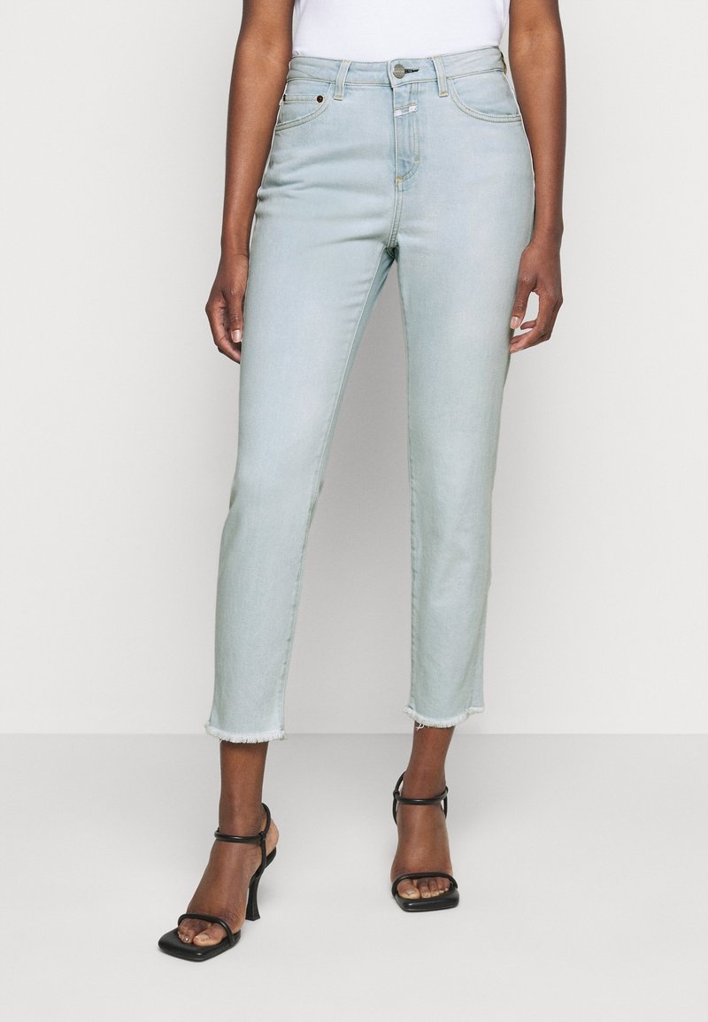 Jean court bleu clair avec ourlets effilochés porté avec des sandales noires à talons hauts et à fines brides, et un top blanc.