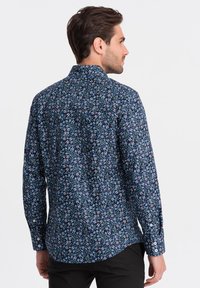 Camicia con bottoni di colore blu navy con un motivo floreale in bianco, rosso e giallo. Caratterizzata da maniche lunghe e colletto. Tessuto di cotone liscio.