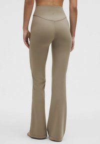 Flared, high-waisted leggings in a muted light brown fabric. Smooth texture with subtle stitching details and a low-profile logo at the waist.