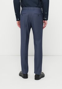 Pantaloni sartoriali blu navy con due tasche posteriori, una texture liscia e una vestibilità dritta, abbinati a scarpe nere.