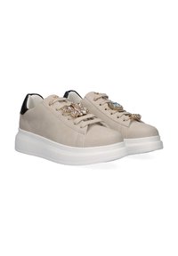 Zapatillas beige con un acabado de cuero suave, que presentan acentos de gemas en los cordones y un detalle trasero negro. Diseño de suela blanca gruesa.