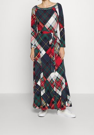 Kvinde iført en langærmet, ankel-lang kjole med et farverigt rødt, grønt, marine og hvidt ternet mønster, kombineret med hvide sneakers.