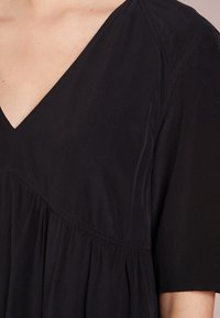 Vestido negro con escote en V, mangas cortas y tejido fruncido bajo el busto para un ajuste holgado. Material suave y ligero con una textura lisa.