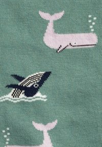 Hellgrüner Stoff mit verspielten Walmotiven in Pink und Schwarz sowie weißen Akzenten. Die Wale zeigen ein Tauchdesign und Luftblasen an der Oberfläche.