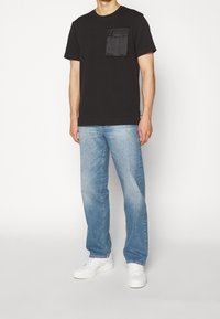 Svart bomulls t-shirt med korta ärmar och en bröstficka. Matcher med ljusblå rakben jeans och vita sneakers.