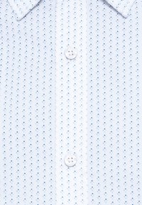 Ανοιχτό μπλε πουκάμισο με μικρό διαμαντένιο μοτίβο. Διαθέτει μυτερό γιακά και κλείσιμο με κουμπιά στο μπροστινό μέρος με λευκά κουμπιά.