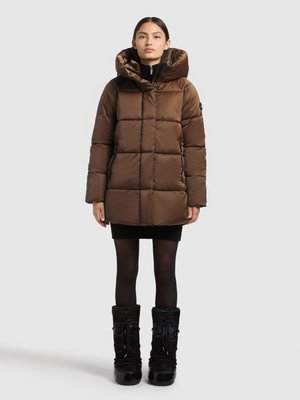 Barna puffert dzseki magas gallérral és csatolt kapucnival, steppelt mintázattal, cipzáros elülső résszel, fekete bordázott ruhára és fekete csizmára viselve.