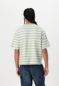 Camiseta de mangas cortas a rayas verdes y blancas hecha de tela texturizada, con un corte relajado y un dobladillo recto.