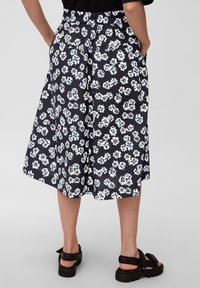 Falda de estampado floral en blanco y negro con acentos en azul, cintura elástica, bolsillos laterales y longitud midi. Tejido ligero, diseño fluido.