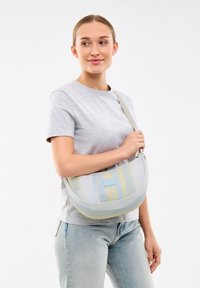 Genomskinlig axelväska i ljusgrått med gula och blå vertikala ränder, slät textur och en liten blå logotypfläck på framsidan.