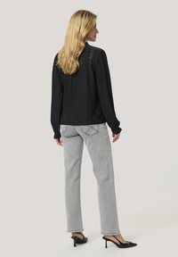 Top nero a maniche lunghe con un motivo testurizzato; abbinato a jeans grigi chiari. Muffin con tacco nero completano l'outfit.