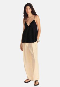 Top nero senza maniche con design a V, tessuto stratificato e vestibilità morbida, abbinato a pantaloni larghi beige chiaro e sandali neri.