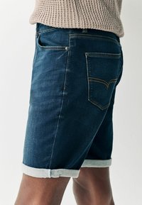 Denim šortsevi u tamnoplavoj boji s prevrnutim rubom. Imaju klasičan dizajn, pet džepova i detalje u žutoj niti. Pamuk s glatkom teksturom.
