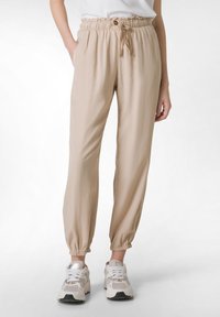 Beige, lehké, tapered tepláky s elastickým pasem a šňůrkou. Mají postranní kapsy a elastické manžety na kotnících.