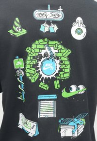 Μαύρη μπλούζα με ποικιλία πολύχρωμων, καρτουνίστικων γραφικών που περιλαμβάνουν πράσινους τοίχους, μάτια, μια αλυσίδα και λογότυπο Nike SB σε μπλε και λευκό χρώμα.