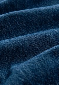 Sügavsinine denimriie, millel on tekstuurne pind ja pehmed voldid. Materjal näitab tüüpilisi kooti mustreid ja kergeid värvitooni variatsioone.