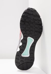 Svart gummisula på sneakers med texturerat grepp. Har en mintgrön accent märkt "TORSION" och ett mönstrat ovandel i rosa och svart.