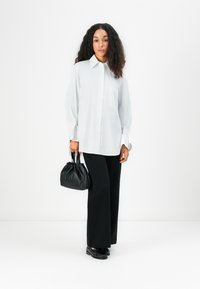 Witte button-down shirt met lange mouwen en een borstzak, gecombineerd met zwarte wijde broek en een kleine zwarte leren handtas.