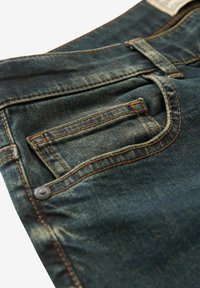 Mørkeblå denimjeans med lys fading, der har orange syninger, en frontlomme og en metalknapdetalje på taljen.