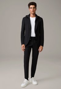 Czarna marynarka z kapturem, biała koszulka i czarne spodnie. Połączone z białymi sneakersami. Gładka tekstura i dopasowany krój.