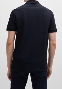 Polo bleu marine en coton lisse, avec un col classique, des manches courtes, et un design minimaliste sans logos ni motifs.