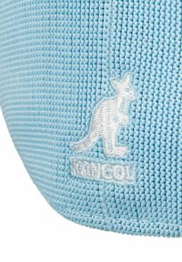 Cappello azzurro chiaro realizzato in tessuto testurizzato, con un logo di canguro ricamato in bianco e il testo "Kangol" vicino al logo.