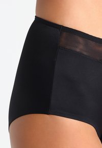 Culottes noires taille haute avec une finition en tissu lisse et des détails en mesh. Présente un bord sans couture pour le confort et un design classique.