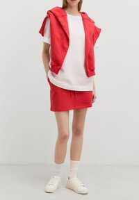 Rode cropped hoodie over een wit T-shirt, gecombineerd met een rode minirok met trekkoord. Gedragen met witte sneakers en sokken.