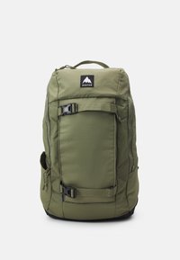 Sac à dos vert olive de forme rectangulaire, avec une poche zippée à l'avant, une poche en maille sur le côté, des bretelles ajustables et des accents en matériel noir.