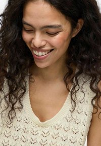 Top de punto en color crema con escote en V, que presenta un patrón de olas texturizadas. Material suave con un tejido abierto y bordes acanalados.